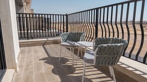 A balcony with two chairs and a table, a black metal railing, and a view of a desert landscape.