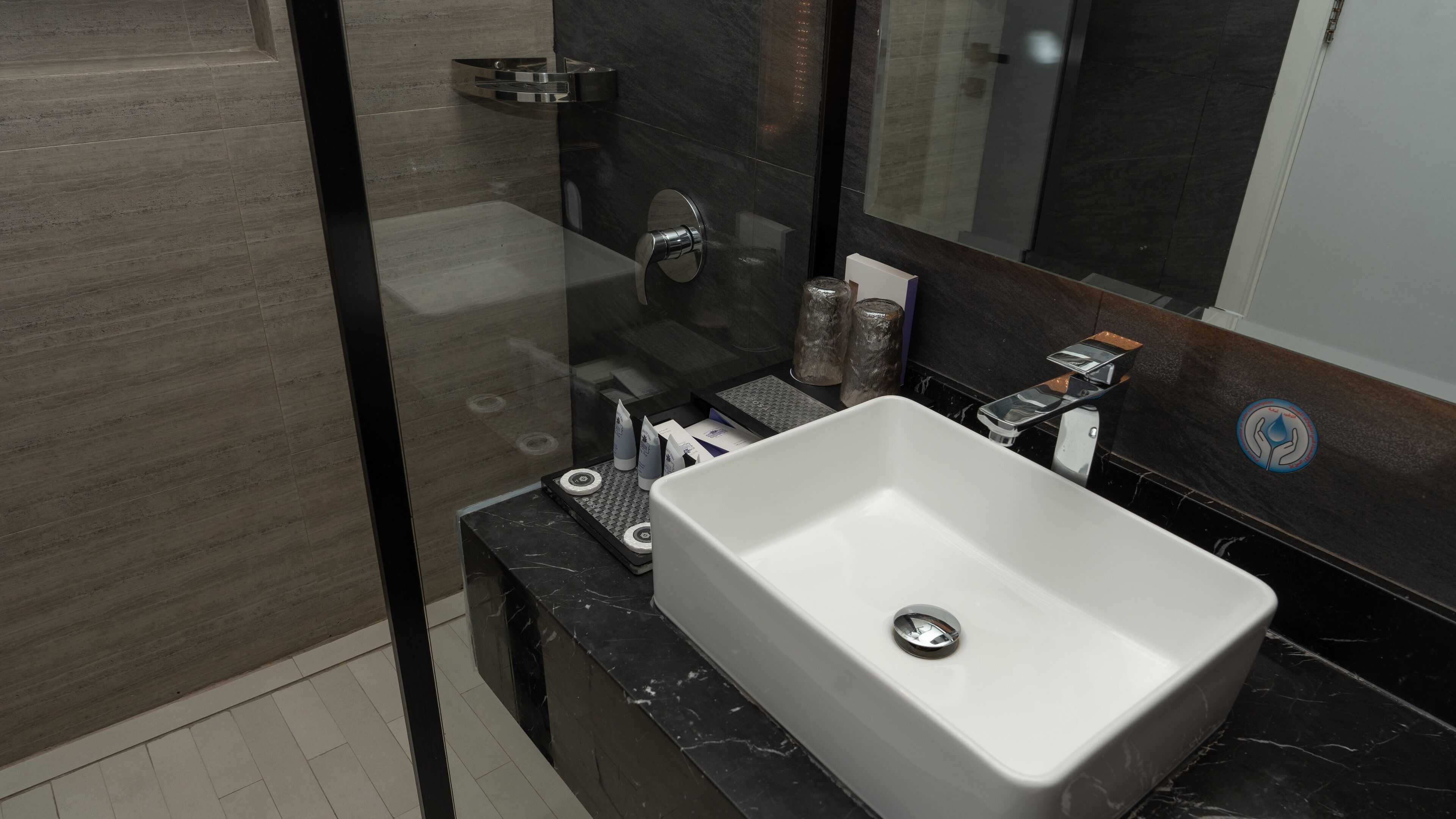 A modern bathroom with a large white sink, a glass shower enclosure, and a dark marble countertop.
