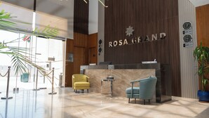 A reception area with a marble floor, two chairs, a reception desk, and a wall-mounted clock. - Rosa Grand Hotel Monsieh (Riyadh)