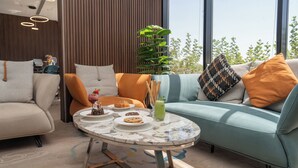A modern living room with a round glass table, two sofas, and a coffee table with various food items. - Rosa Grand Hotel Monsieh (Riyadh)