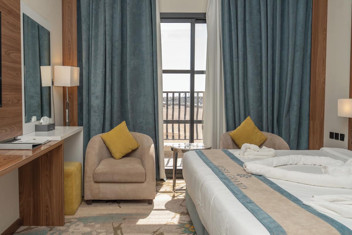 A hotel room with a desk, two chairs, a bed, and a balcony view.