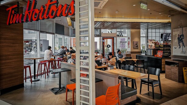 Un restaurant Tim Hortons doté d’un intérieur moderne, comprenant un bar, des espaces de repos et un panneau d’affichage où le menu est clairement visible.