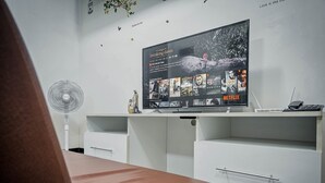Une chambre moderne avec un grand téléviseur à écran plat fixé sur un meuble blanc, un petit ventilateur et un élément décoratif mural.
