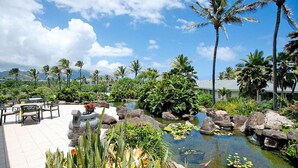 A tropical resort with a pool surrounded by rocks and palm trees, outdoor seating, and lush greenery.