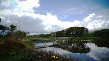 A bridge over a calm body of water with lush greenery and a cloudy sky.