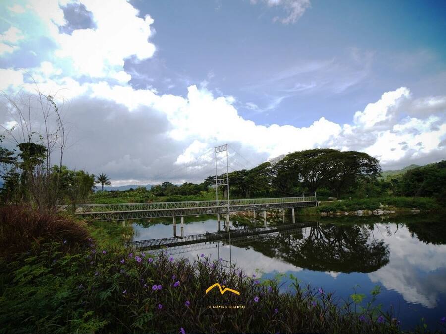A bridge over a calm body of water with lush greenery and a cloudy sky.