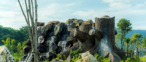 A waterfall cascading over a rocky structure surrounded by lush greenery and palm trees.