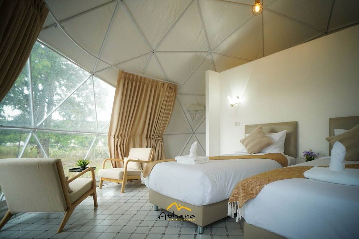 A modern, spacious room with a large window, a comfortable chair, two beds, and a small table with a plant.