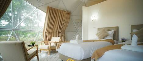 A modern, spacious room with a large window, a comfortable chair, two beds, and a small table with a plant.