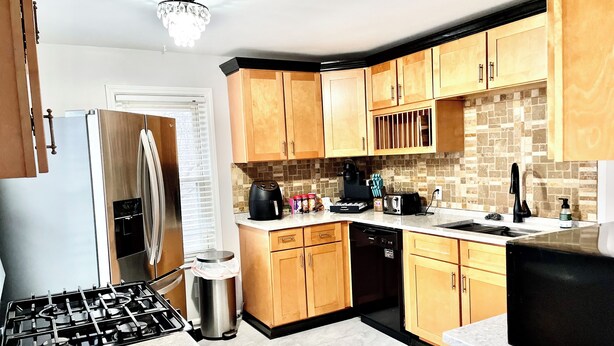 A modern kitchen with wooden cabinets, a stainless steel refrigerator, a gas stove, and a dishwasher.