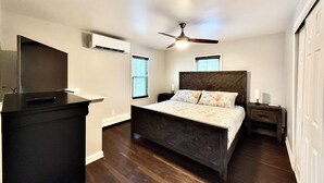 A bedroom with a bed, a ceiling fan, a TV, and a dresser.