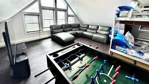 A loft-style room with a sectional sofa, a foosball table, and a ceiling fan.