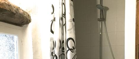 A bathroom with a shower, a toilet, and a window.