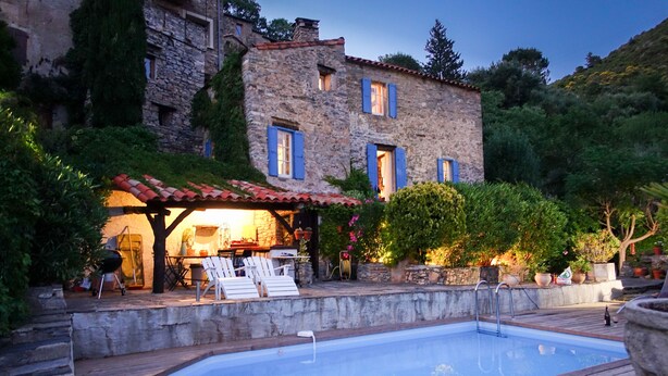 A stone building with a pool, outdoor seating, and a barbecue area.