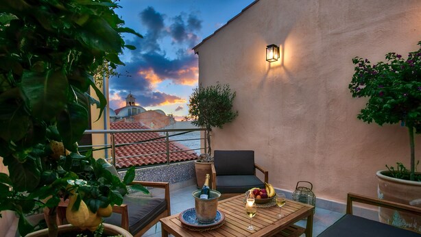 A rooftop terrace with a wooden table, chairs, potted plants, and a view of a building with a dome.