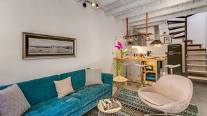 A modern living room with a teal sofa, a round coffee table, and a pink armchair. A framed black and white photograph is on the wall.