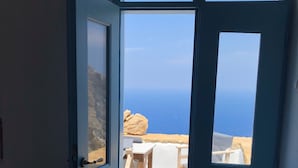 An open door leading to a balcony with a view of the sea and rocky landscape.