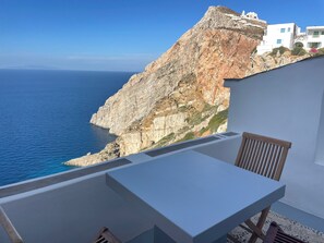 En balkon med et bord og en stol med udsigt over en klippe og havet.