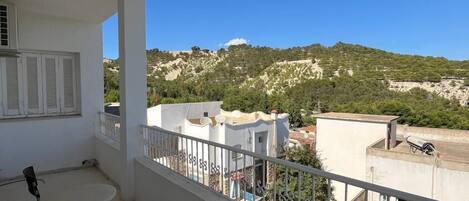 Un balcón con mesa y sillas, con vistas a un paisaje montañoso y edificios.