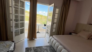 Une chambre à coucher comprenant un lit, une table de chevet, un luminaire suspendu et une vue sur l’extérieur grâce à une porte coulissante.