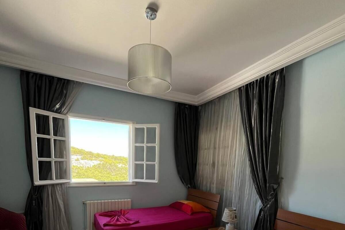 Ein Schlafzimmer mit zwei Betten, einem Fenster mit Vorhängen, einem Heizkörper und einer Deckenleuchte.