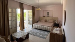Une chambre à coucher comprenant un lit, une table de chevet, une chaise, une petite table, une lampe et une vue sur l’extérieur.