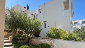 Une cour avec des marches en pierre menant à un bâtiment blanc, entouré de verdure et d’un mur de pierre.