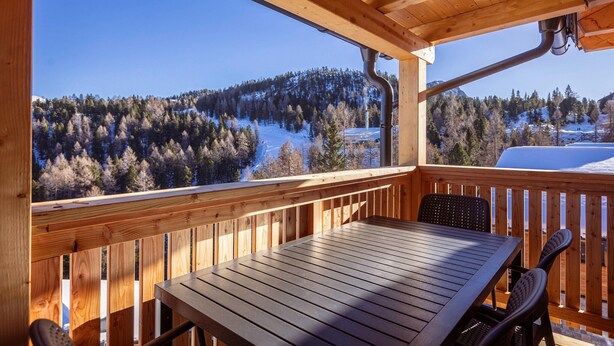A wooden deck with a table and chairs, overlooking a snowy landscape with trees and a clear blue sky. - Holiday Apartment near ski slope (Turracher Höhe)