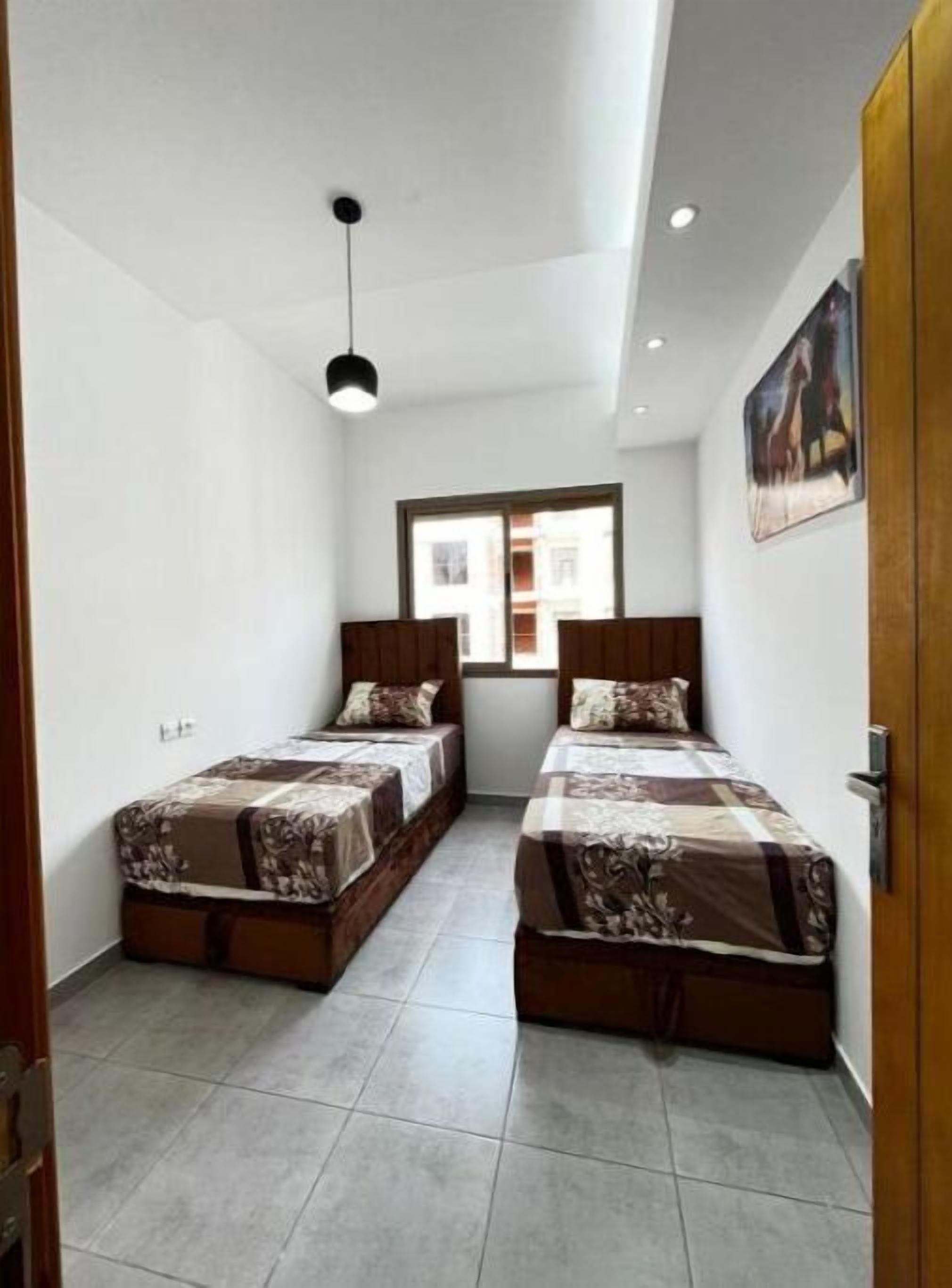 Una habitación pequeña y bien iluminada con dos camas, una ventana y una puerta.