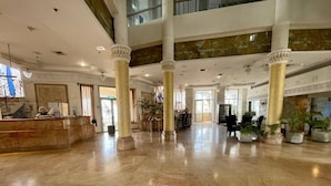 Un hall d’entrée spacieux, doté de sols en marbre, de grandes colonnes et d’un comptoir d’accueil.