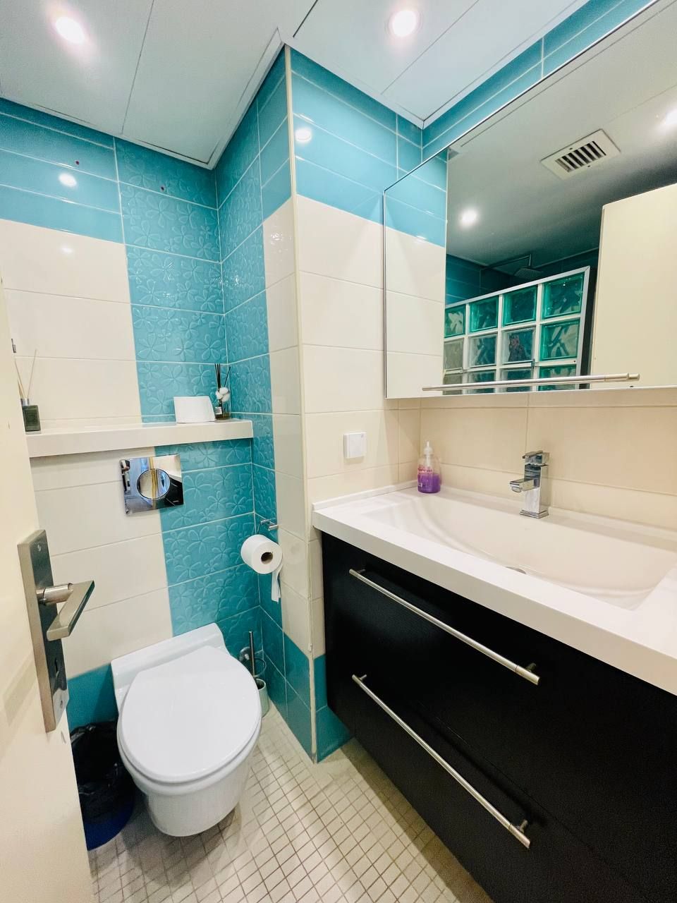 Un baño con inodoro blanco, un lavabo con espejo arriba y azulejos blancos y azules en las paredes.