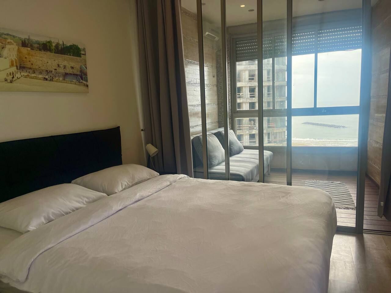 A hotel room with a large bed, a view of the sea through floor-to-ceiling windows, and a balcony with a view of the sea.