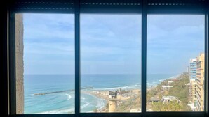 Une vue sur la côte, aperçue à travers une fenêtre, avec une plage, l’océan et des bâtiments.