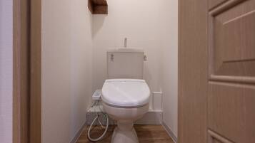 A small, clean bathroom with a white toilet, a wooden floor, and a wall-mounted shelf.