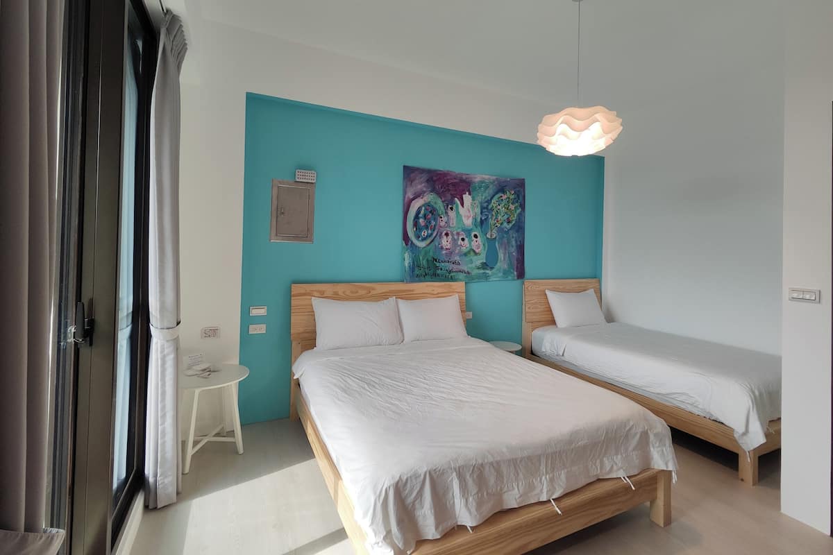 Quarto com duas camas, uma parede em tom de verde-água, um quadro colorido e uma luminária pendente.