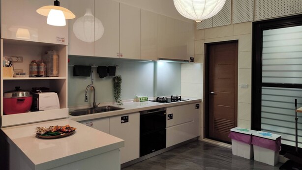 A modern kitchen with white cabinetry, a stainless steel sink, a gas stove, and a red rice cooker. There are two pendant lights and a hanging paper lantern. - Nan Ping Ourhill B&B (Dongshan)