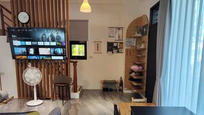 A modern living room with a flat-screen TV displaying various streaming services, a wooden slat wall, a fan, a small seating area, and a shoe rack. - Nan Ping Ourhill B&B (Dongshan)