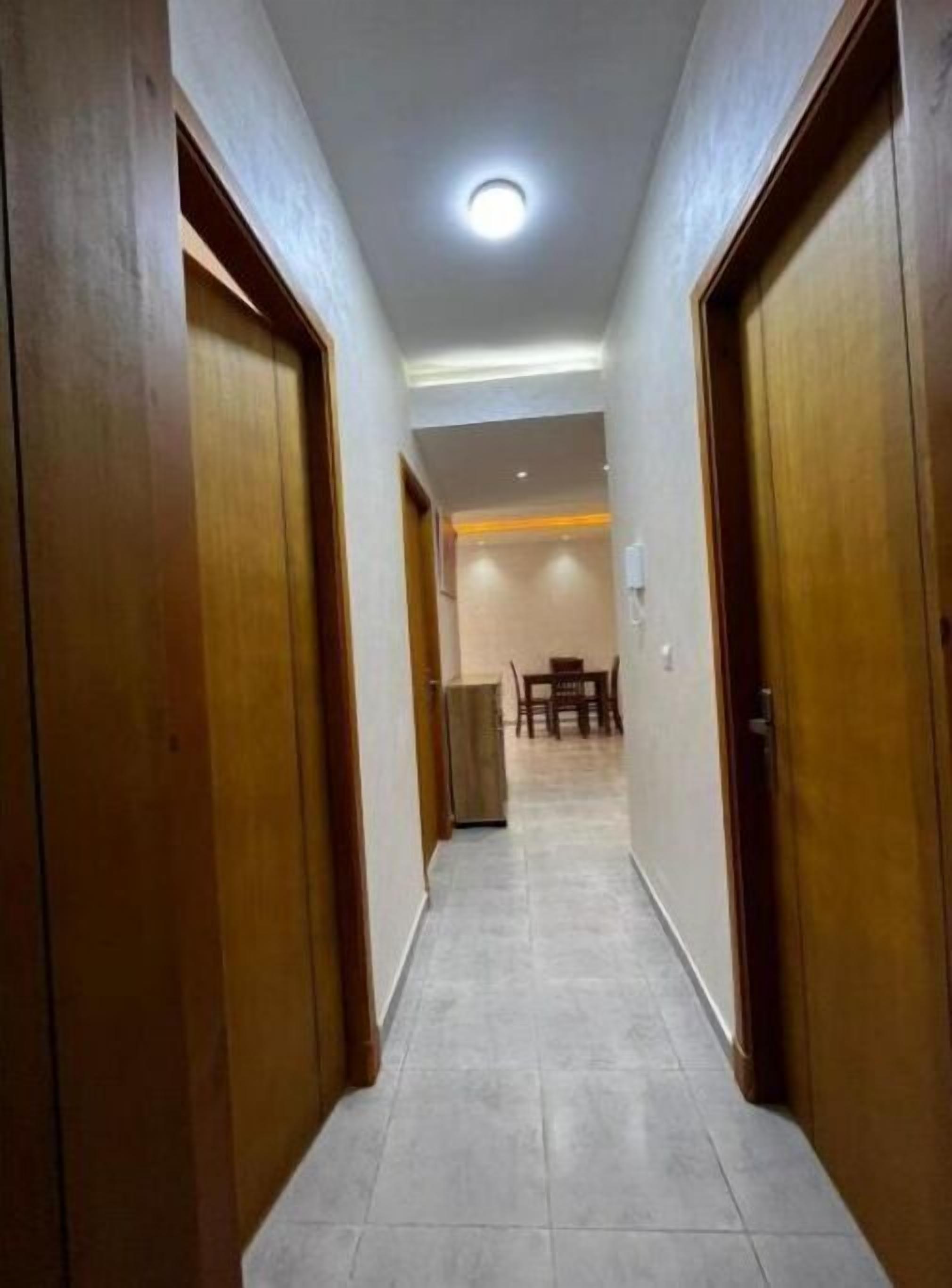 A hallway with wooden doors, a tiled floor, and a dining area with a table and chairs in the distance.