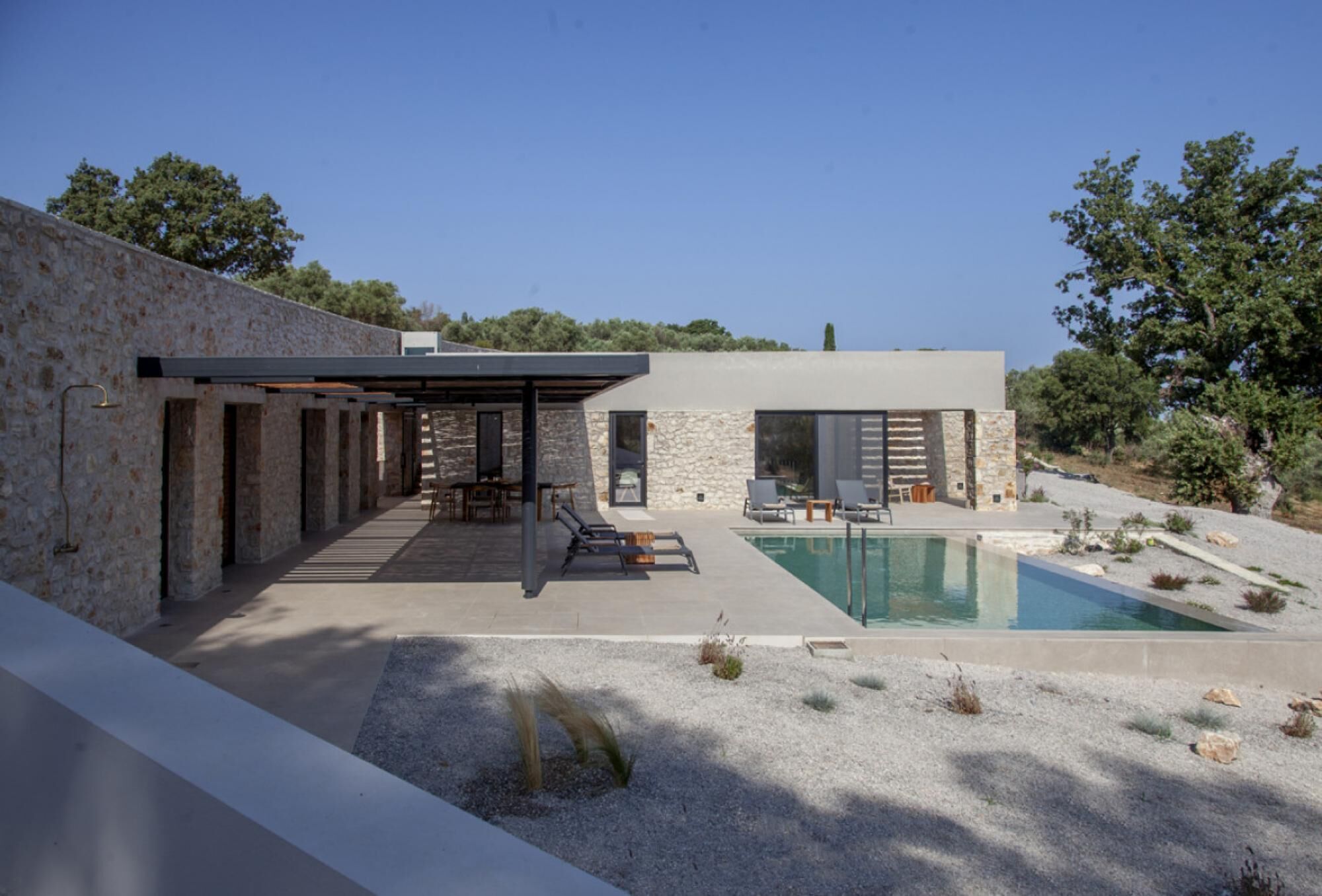A modern outdoor pool area with a stone wall, lounge chairs, and a pergola.