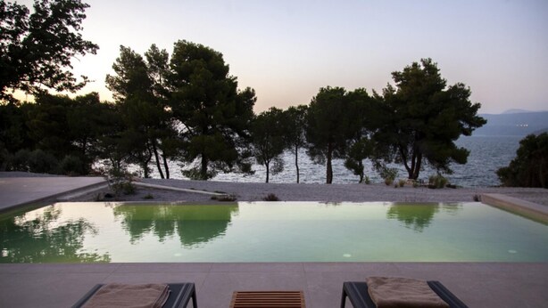 Una piscina con dos tumbonas y una mesa de madera, rodeada de árboles y vistas al mar.