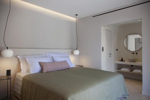 A modern bedroom with a bed, bedside lamps, a nightstand, and a bathroom visible through an open door.