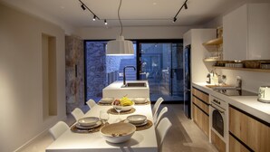 A modern kitchen with a dining area, featuring a central island, built-in appliances, and a view through the glass door.