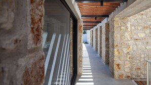 A corridor with stone walls and wooden beams, leading to a glass door.