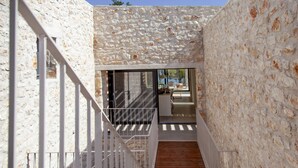 A narrow stone-walled corridor with a wooden staircase leading to a balcony.