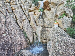 Eine natürliche Felsformation mit einem kleinen Wasserfall und einer mit „VODKA STUFS“ beschrifteten Wasserflasche, die auf einem Felsen platziert ist.