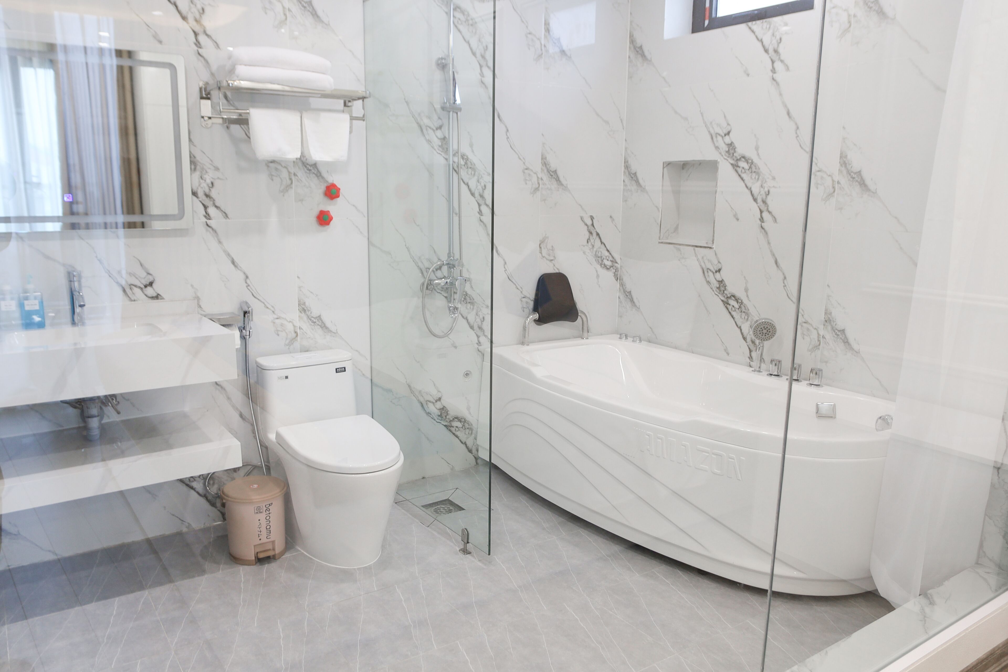 Un baño moderno con inodoro blanco, ducha con mampara de vidrio y una bañera grande.