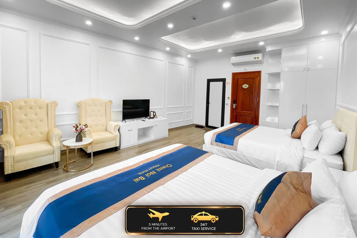 Habitación de hotel con dos camas, televisor, escritorio y silla. Señalización indica a 5 minutos del aeropuerto y servicio de taxi las 24 horas, los 7 días.