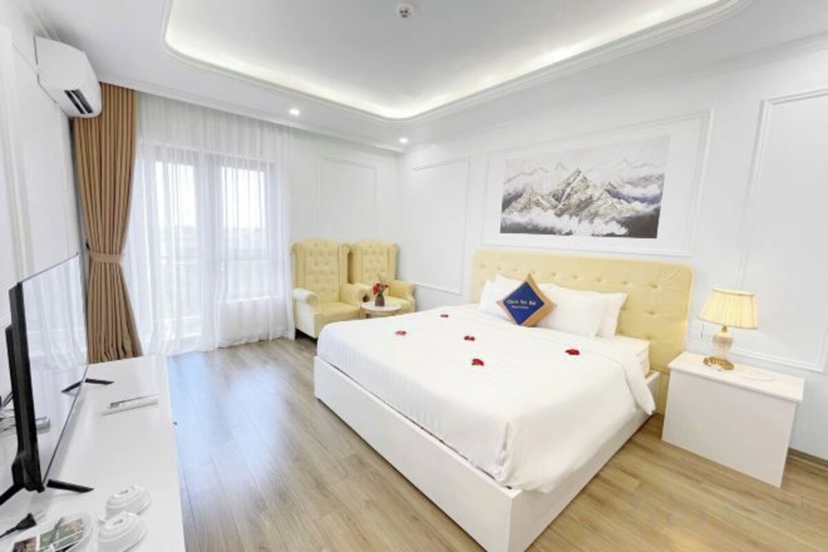 Una habitación de hotel con una cama grande, una mesita de noche, un televisor y una ventana con cortinas.