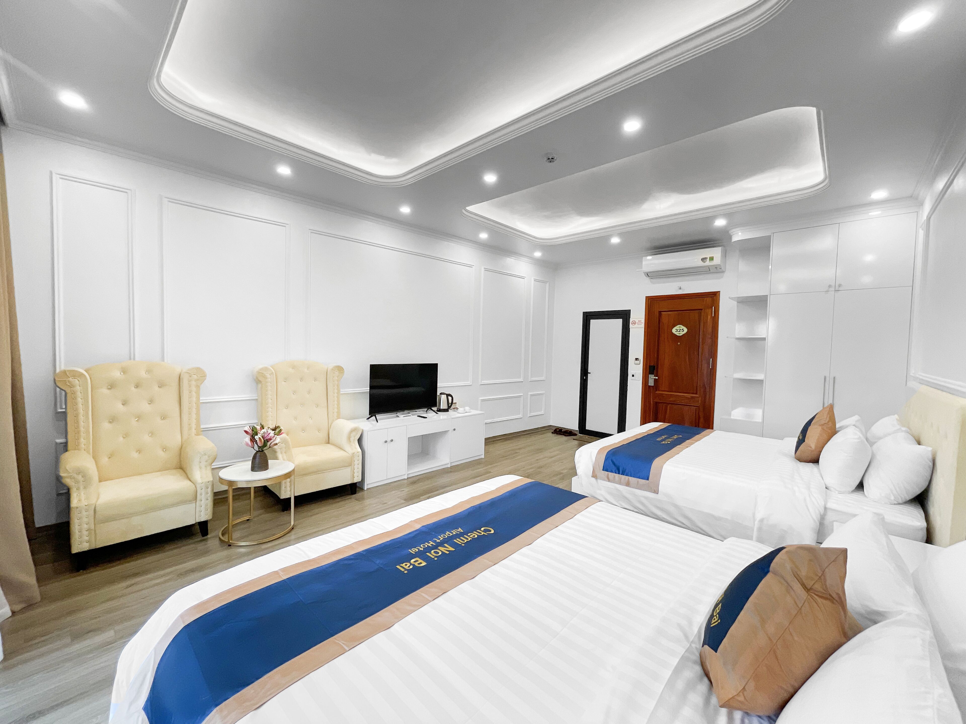 Une chambre d’hôtel avec deux lits, une télévision, un bureau et deux fauteuils.