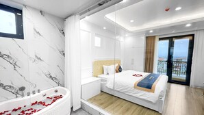 Una habitación de hotel moderna con una cama grande, una bañera con pétalos de rosa, un balcón con vistas y paredes de mármol.